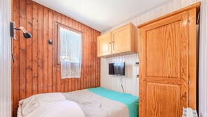 Ett rum med träpanel på väggarna, en säng med vitt och grönt sänglinne, en trägarderob och en tv som är monterad ovanför den.