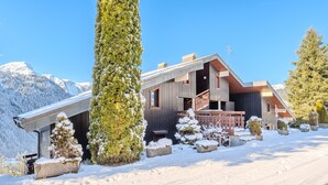 En modern skidort med en byggnad som har en träfasad, ett takförsett utomhusområde samt snötäckta träd och växter.