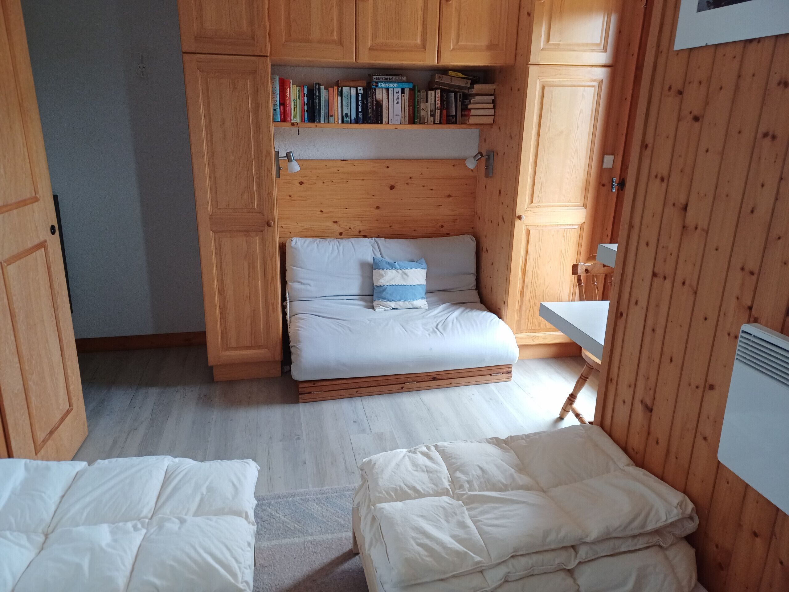 A compact room with a bed, a small desk, and wooden cabinets.