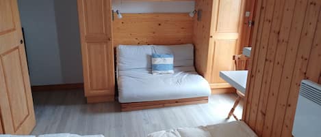 A compact room with a bed, a small desk, and wooden cabinets.
