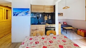 Een kleine keuken met houten kastjes, een inbouwoven en een eethoek met een tafel en stoelen.