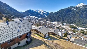 Een bergdorp met traditionele huizen, een heldere lucht en besneeuwde bergtoppen op de achtergrond.