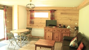 Une pièce confortable, aménagée comme un chalet, avec un intérieur en bois, une table à manger avec des chaises, un canapé et un téléviseur posé sur un meuble en bois.