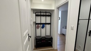 Un couloir avec un présentoir en métal noir où sont rangées les chaussures et un petit tapis sur le sol.