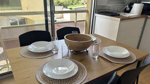 Une table à manger dressée avec de l’argenterie blanche, des verres transparents et un saladier en bois, offrant une vue sur l’extérieur grâce à de grandes fenêtres.