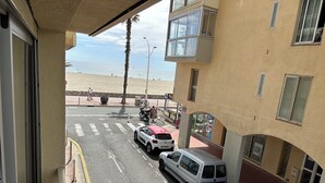 Une vue de rue avec des voitures garées, un passage piéton et une plage en arrière-plan.