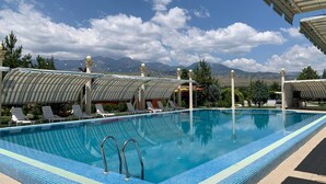 A swimming pool with lounge chairs and umbrellas, surrounded by mountains and clear skies.
