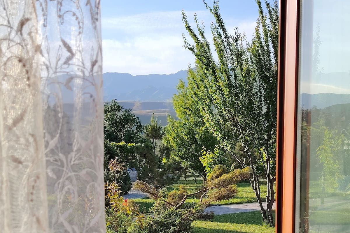 A window with a view of a landscaped garden, a paved area, and distant mountains.