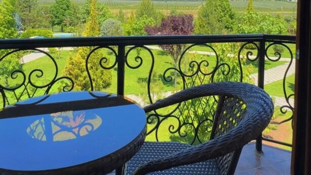A balcony with a table and chairs, offering a view of a green landscape and distant hills.
