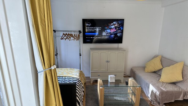 Ein Wohnzimmer mit an der Wand montiertem Fernseher, einer Couch, einem Couchtisch und einem Kleiderschrank.