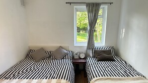 Ein Schlafzimmer mit zwei Betten, jeweils mit gestreifter Bettwäsche, einem Nachttisch mit einer Uhr und einem Schild, sowie einem Fenster mit Vorhängen.