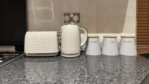 Eine Küche mit einem Gasherd, einer Kaffeemaschine und drei Behältern, beschriftet mit Zucker, Tee und Kaffee.