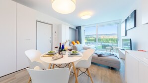 Ein moderner Essbereich mit einem runden Tisch, weißen Stühlen und Blick ins Freie durch große Fenster.
