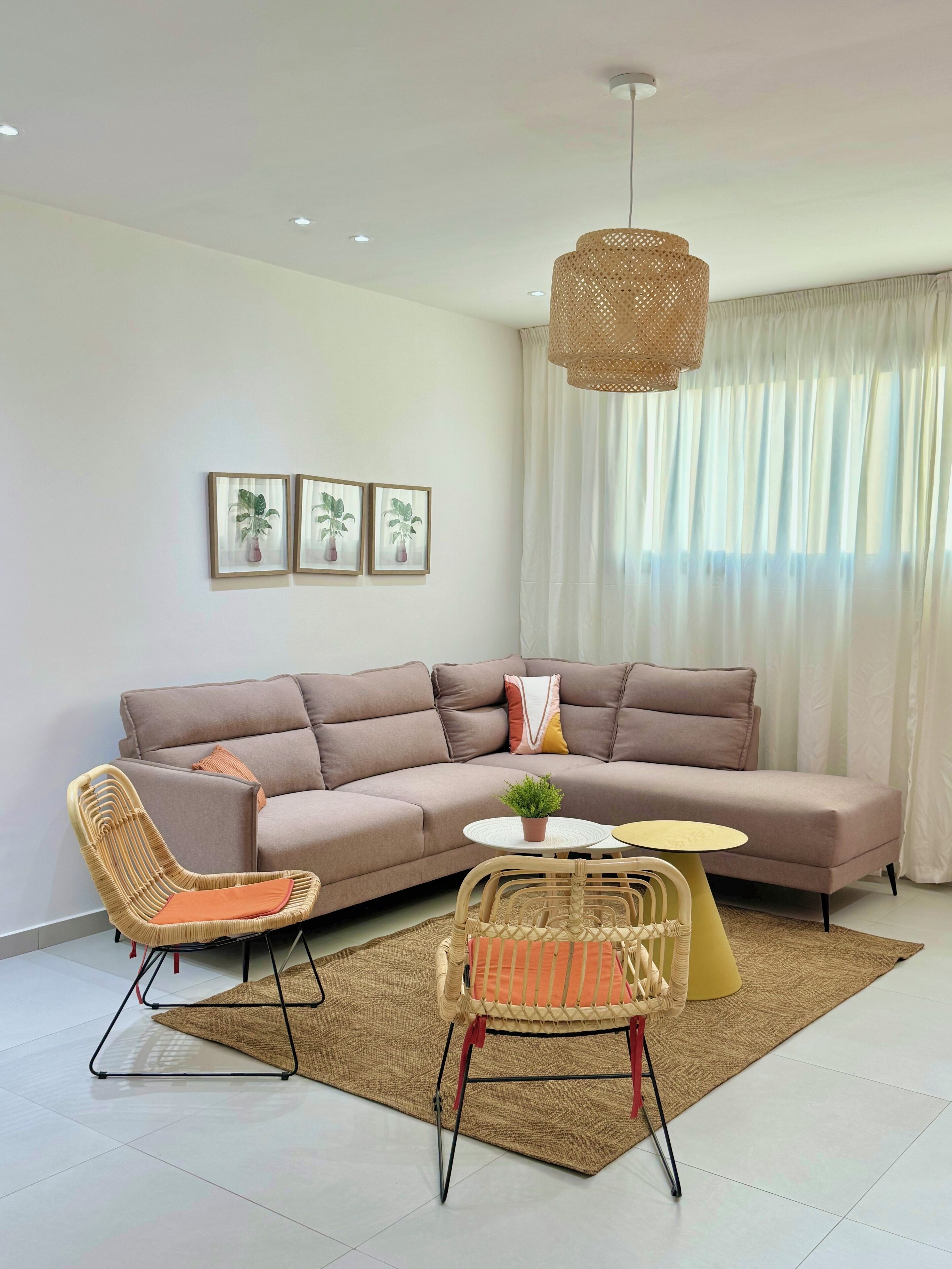 A modern living room with a sectional sofa, two wicker chairs, a round coffee table, and a hanging light fixture.