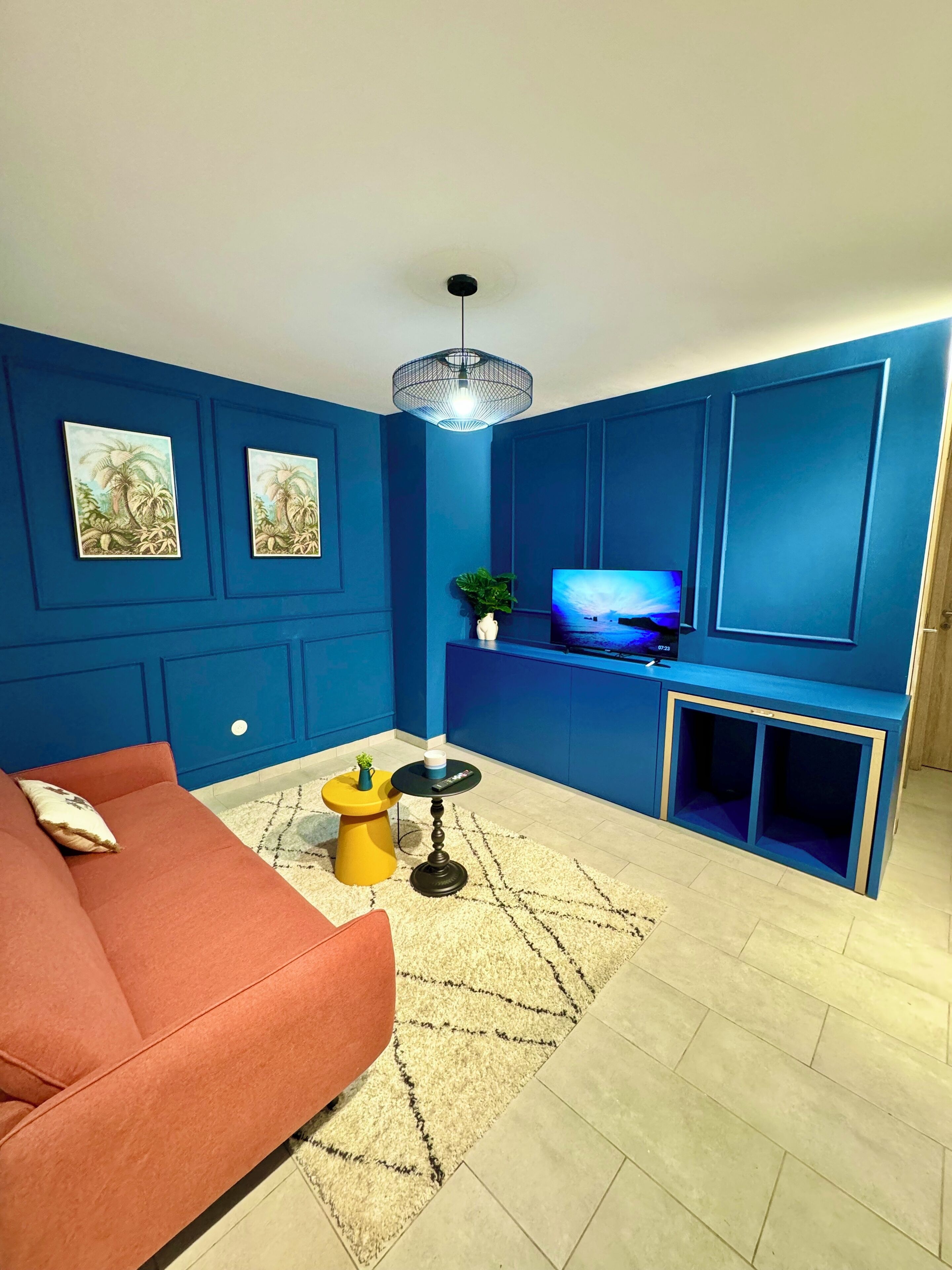 A living room with a blue wall, a red sofa, a yellow side table, a black coffee table, a TV, and a plant.