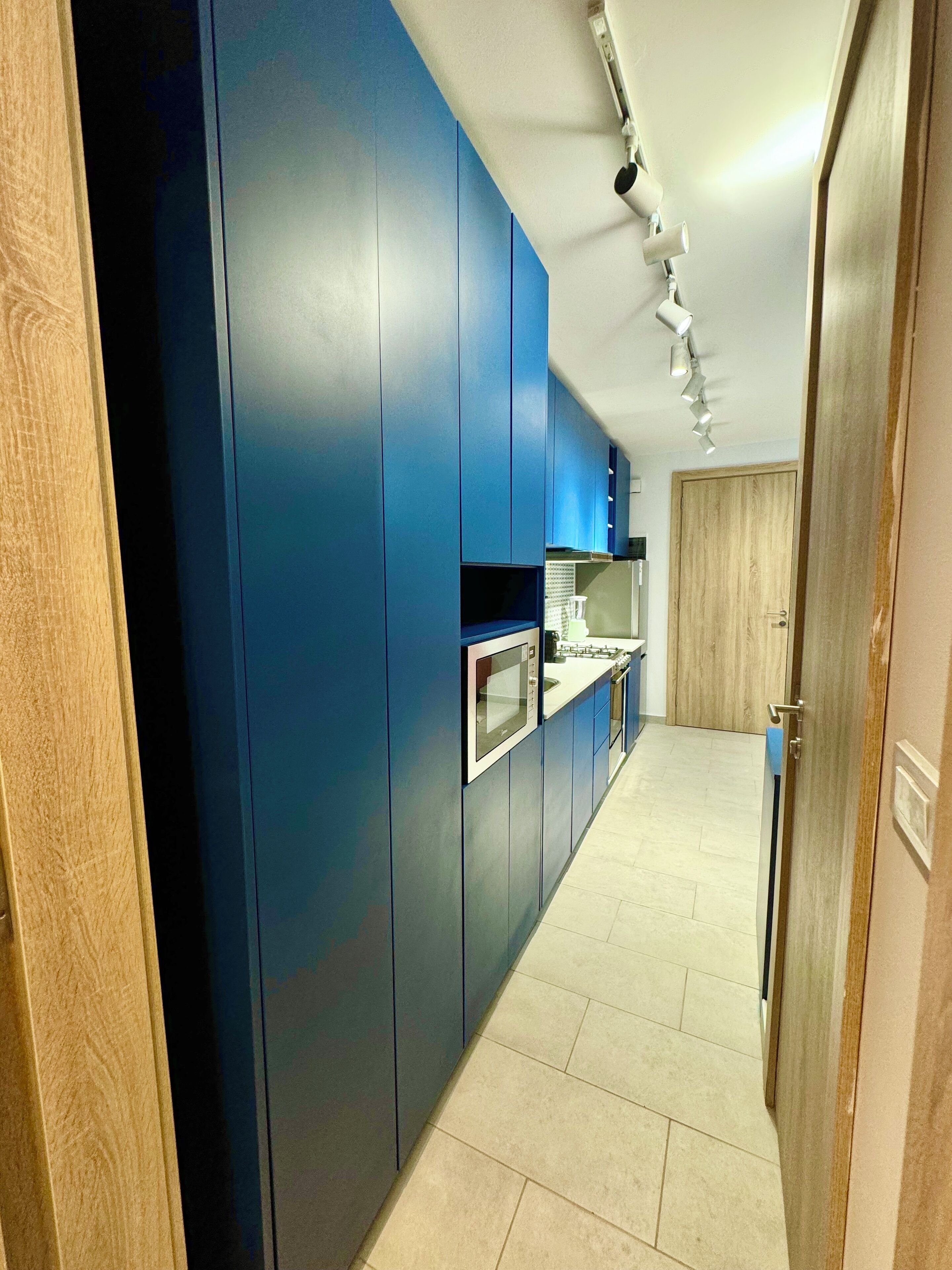 A narrow hallway with blue cabinets, a stainless steel oven, and a wooden door.