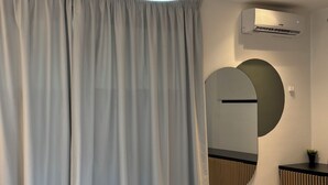 A modern bedroom with a bed, a hanging light fixture, a wall-mounted air conditioner, and a large mirror. - KIA ORA APPART HOTEL (Abidjan)