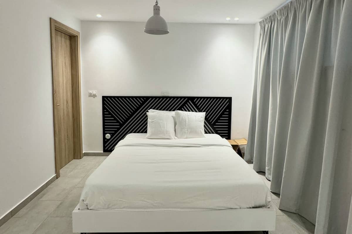 A modern bedroom with a large bed, a wooden door, a black headboard, and a grey curtain.