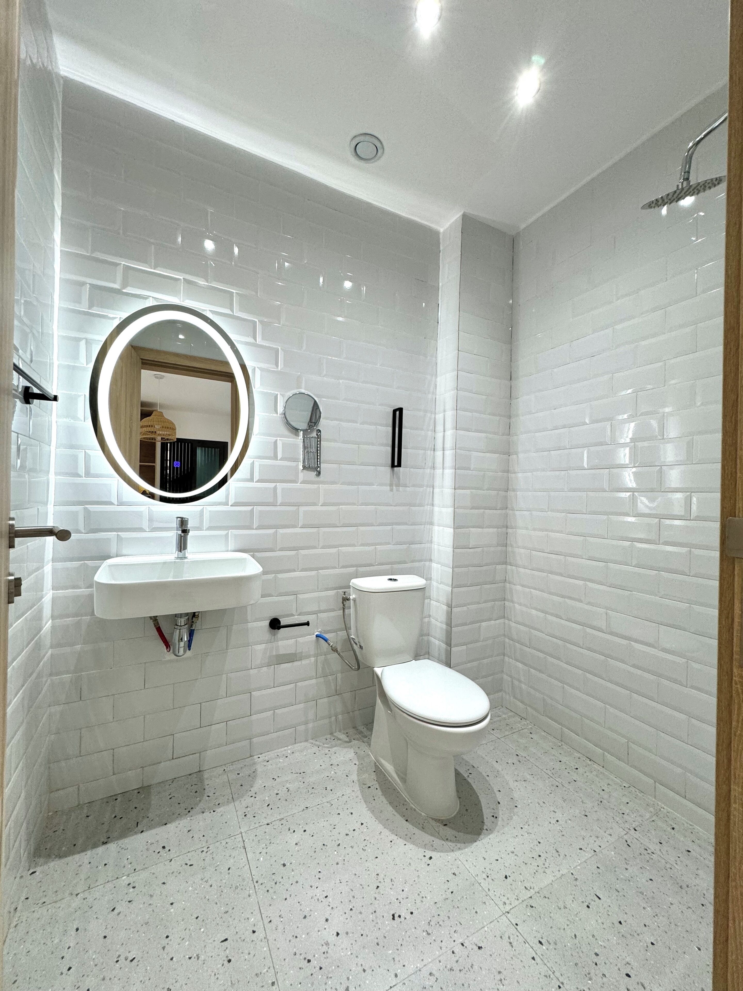 A modern bathroom with white subway tiles, a round mirror, a toilet, and a shower.