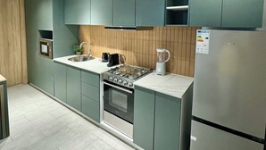 A modern kitchen with teal cabinets, a stainless steel refrigerator, a built-in oven, and a gas stove. - KIA ORA APPART HOTEL (Abidjan)