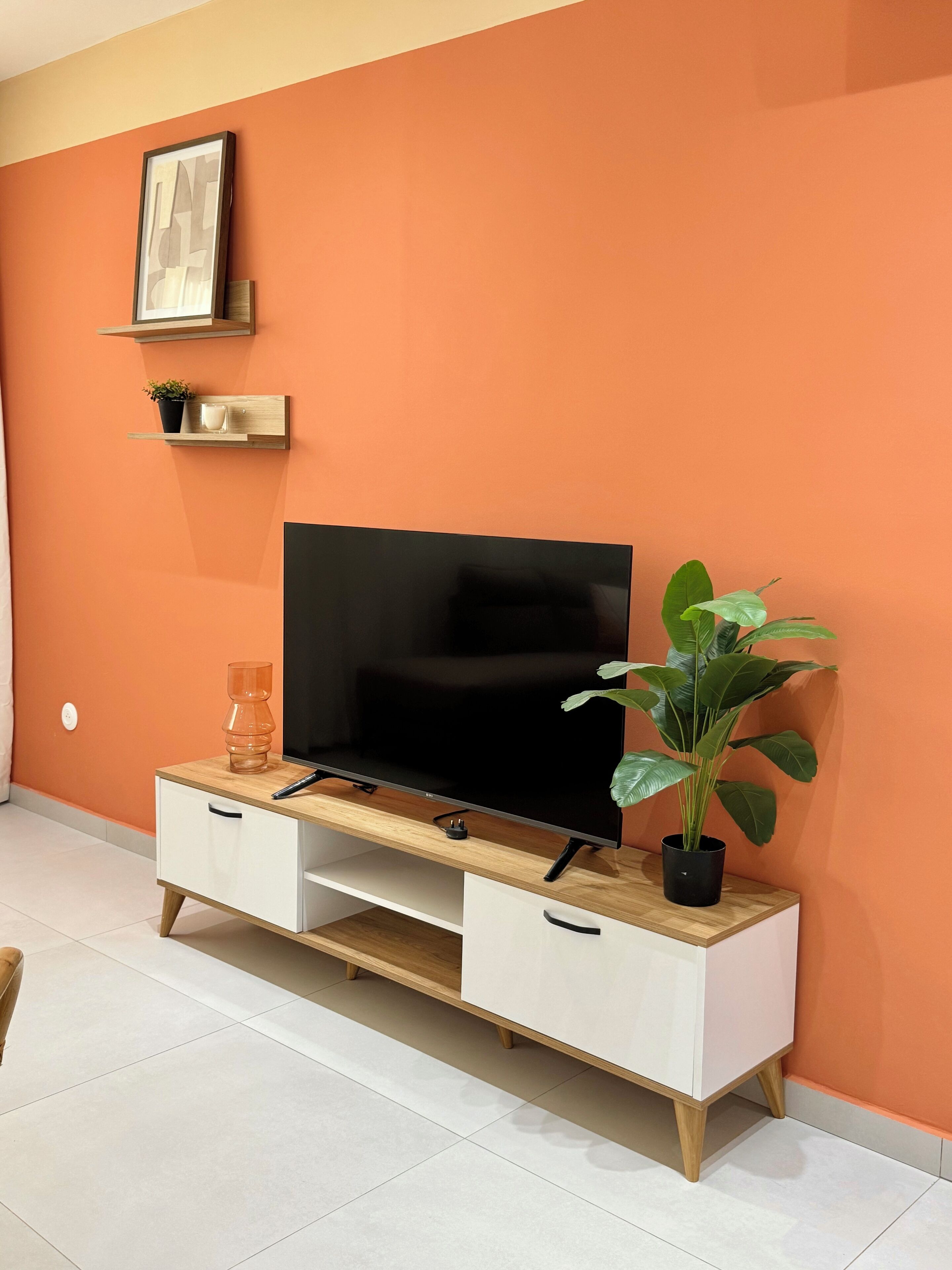 Una sala de estar moderna con una televisión de pantalla plana sobre un mueble de madera, una planta en maceta y un cuadro en la pared.
