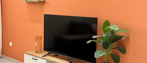 Una sala de estar moderna con una televisión de pantalla plana sobre un mueble de madera, una planta en maceta y un cuadro en la pared.