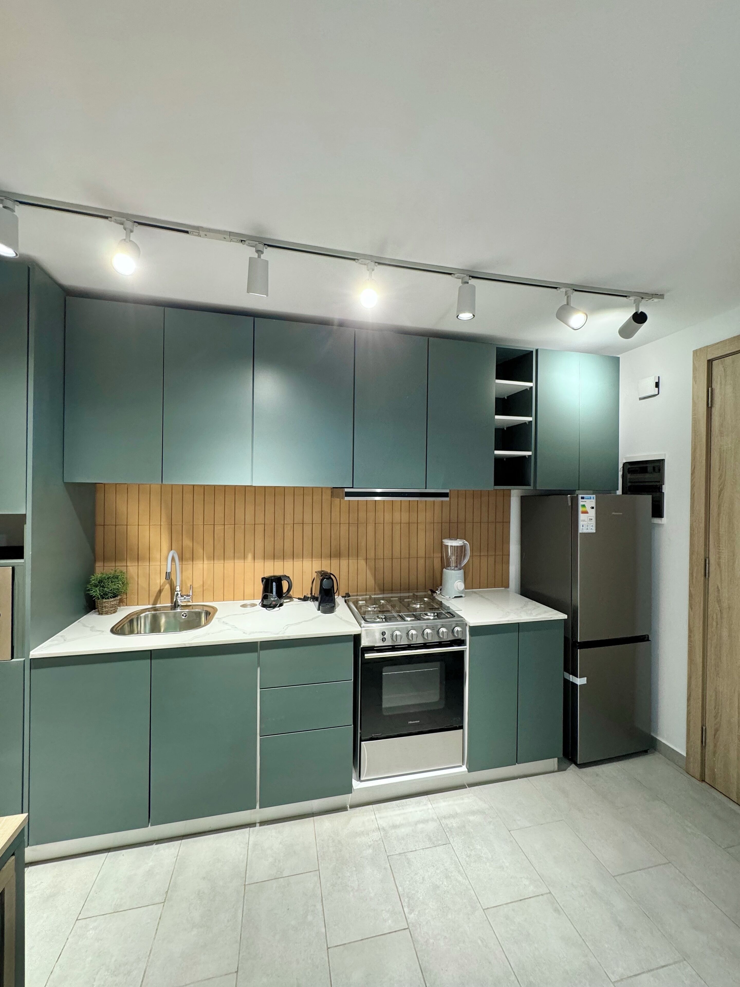 Une cuisine moderne avec des armoires de couleur turquoise, un évier en acier inoxydable, une cuisinière à gaz et un réfrigérateur.