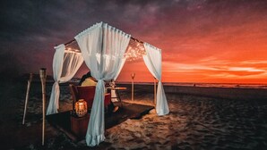 Une tente installée sur la plage, avec une table et des chaises, le tout mis en valeur par le décor d’un coucher de soleil.