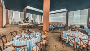 Un vaste espace de restauration intérieur, doté de tables et de chaises rondes, de grandes fenêtres et d’un plafond haut.