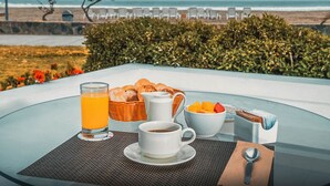 Une table en verre, dressée pour le petit-déjeuner, avec vue sur la plage et l’océan.