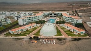 Vue aérienne d’un hôtel composé de plusieurs bâtiments, doté d’une piscine centrale et d’une grande structure en forme de serre.