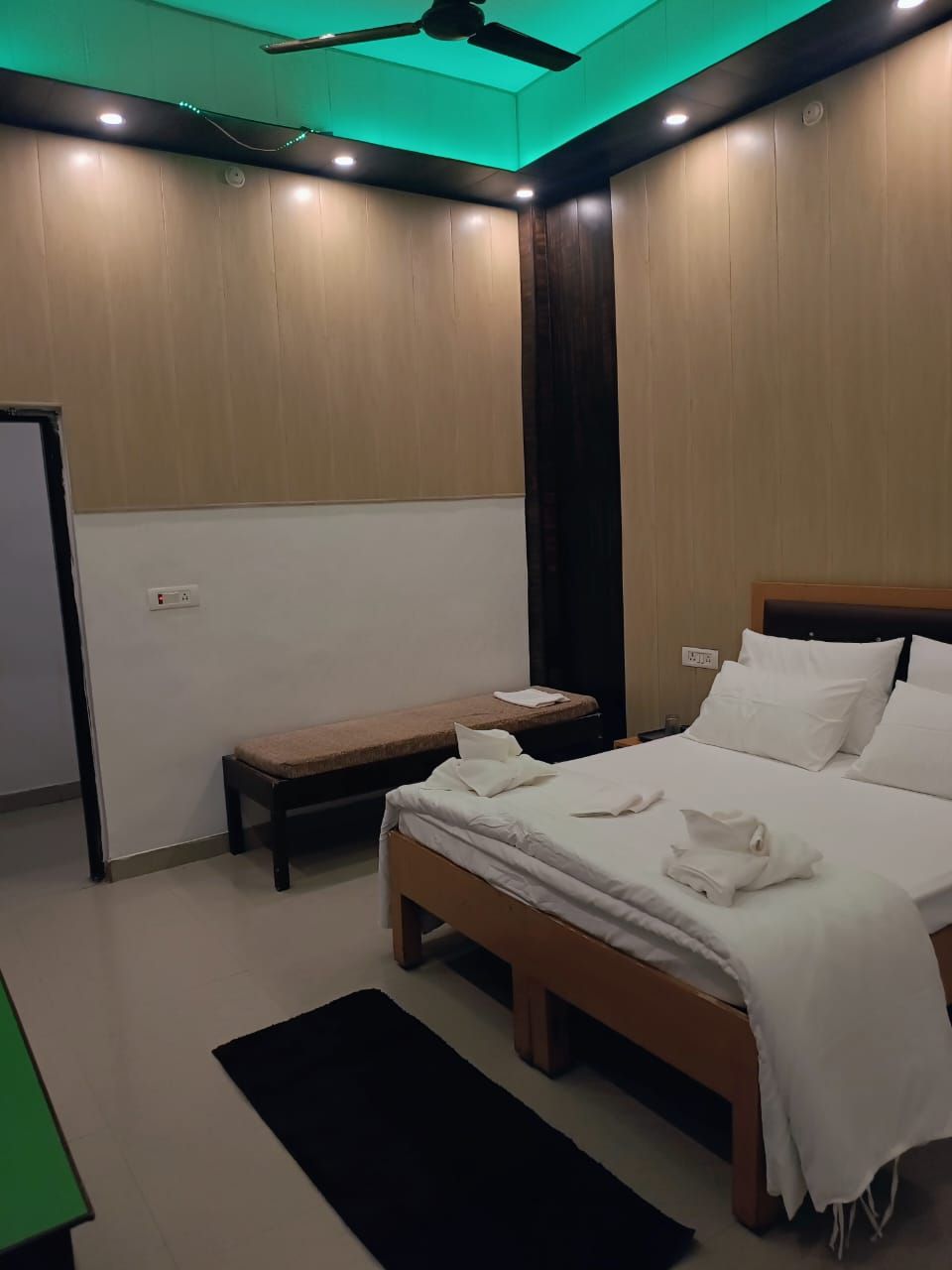 Een moderne slaapkamer met een bed, nachtkastje, bankje en een plafondventilator.