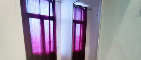A room with a large mirror, a small rug, and a window with purple curtains.