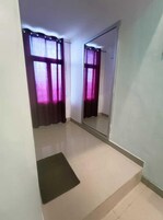 Una habitación con un espejo grande, una alfombra pequeña y una ventana con cortinas moradas.