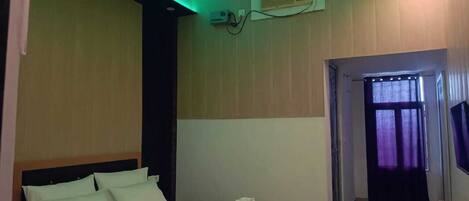 A bedroom with a bed, ceiling fan, air conditioning unit, and a view of the outside through a window with curtains.