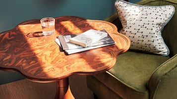 A room with a wooden table, a green armchair, a lamp, and a glass of water.