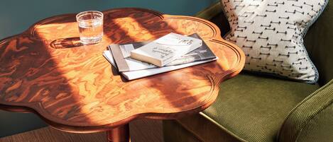 A room with a wooden table, a green armchair, a lamp, and a glass of water.