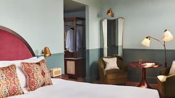 Habitación de hotel con una cama grande, dos sillones, una mesita, un espejo, un armario y una lámpara.