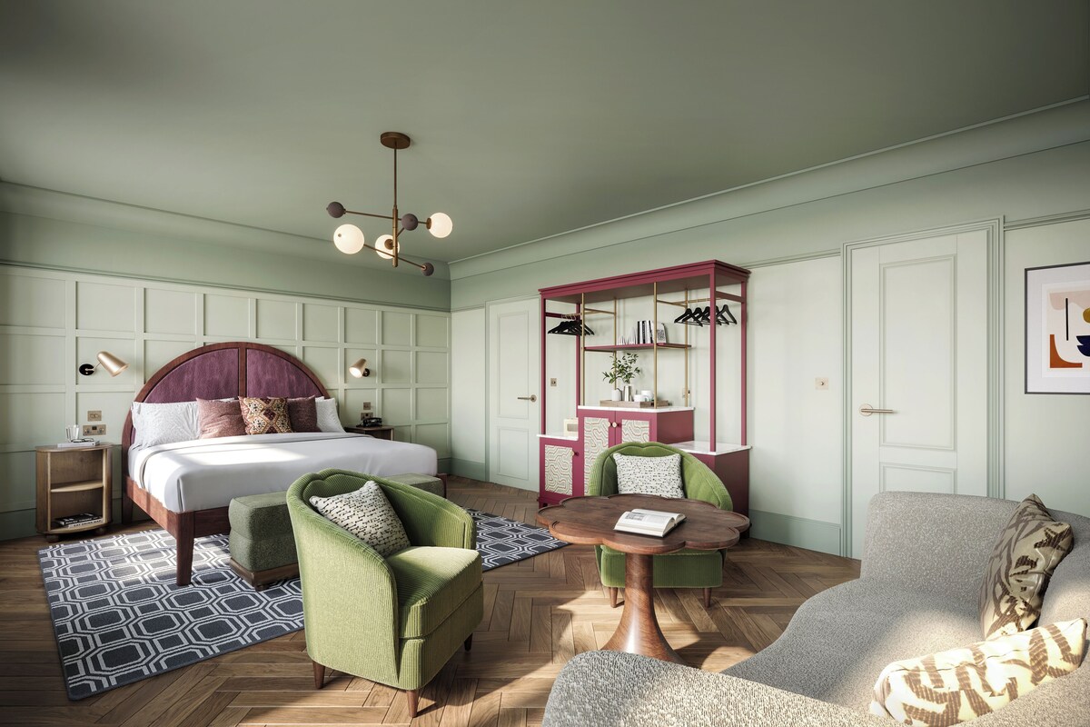 A bedroom with a bed, two chairs, a small table, a wardrobe, and a nightstand.