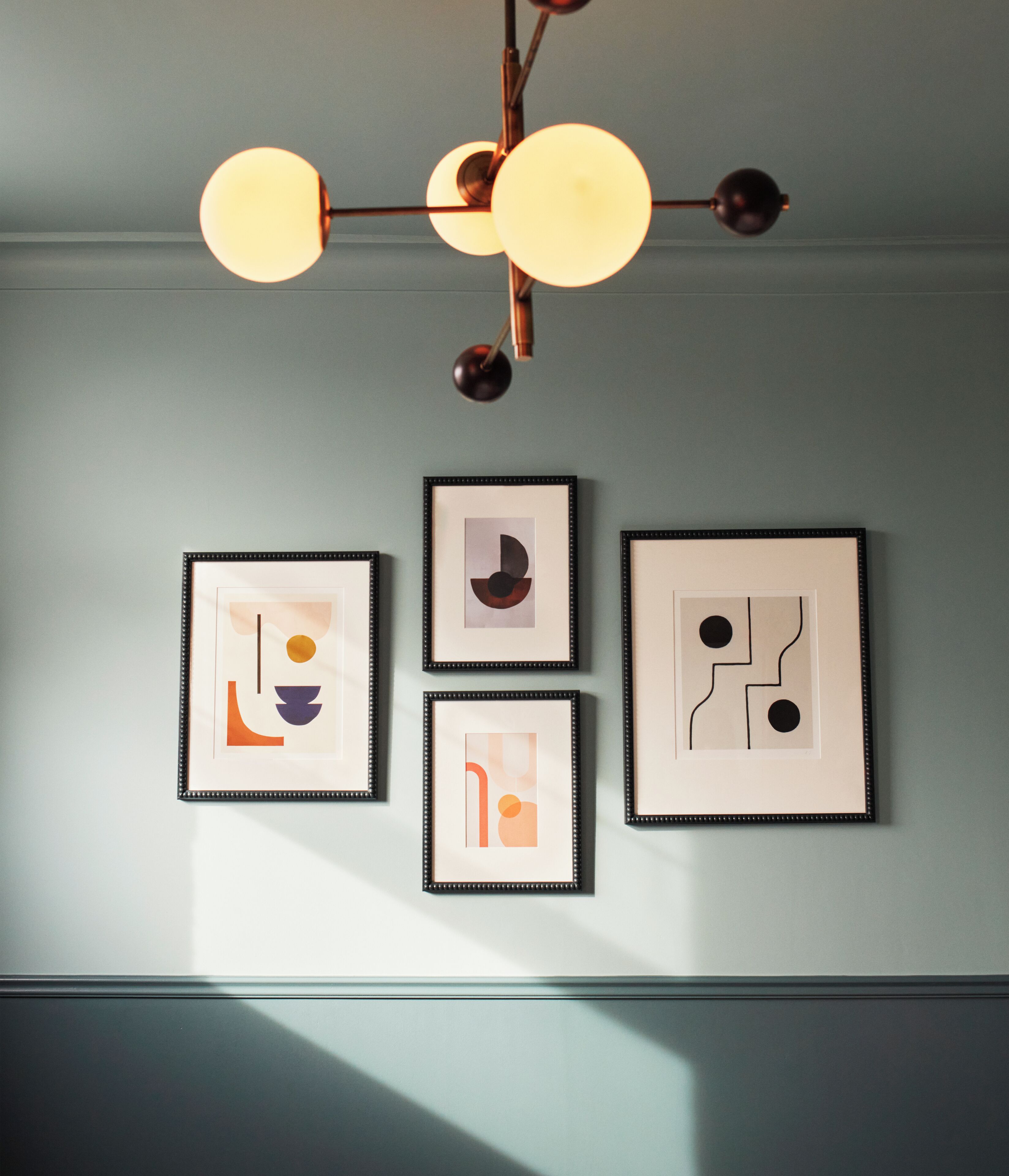 Un mur orné de quatre œuvres d’art abstraites encadrées et d’un lustre moderne.