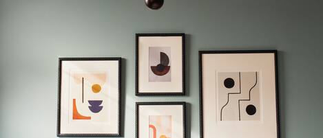 A wall with four framed abstract artworks and a modern chandelier.