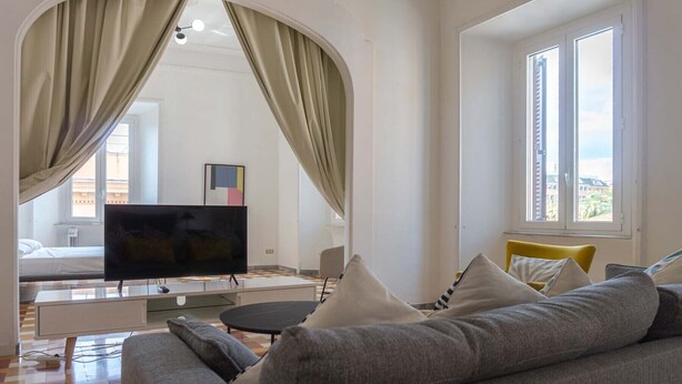Una sala de estar moderna con un sofá, un televisor, una mesa de comedor y vistas de la ciudad a través de amplias ventanas.