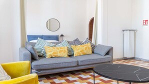 Una sala de estar moderna con un sofá gris, cojines amarillos y estampados, un espejo redondo y una mesa de centro negra.