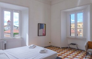 A hotel room with a bed, a chair, a radiator, and a window with a view of buildings. - Villa Borghese Large Apartment (Rome)