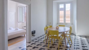 Una habitación con cama, una mesa con sillas, una ventana y piso de baldosas.