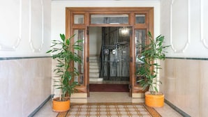 Un pasillo con puerta de madera, plantas en macetas y suelo estampado.