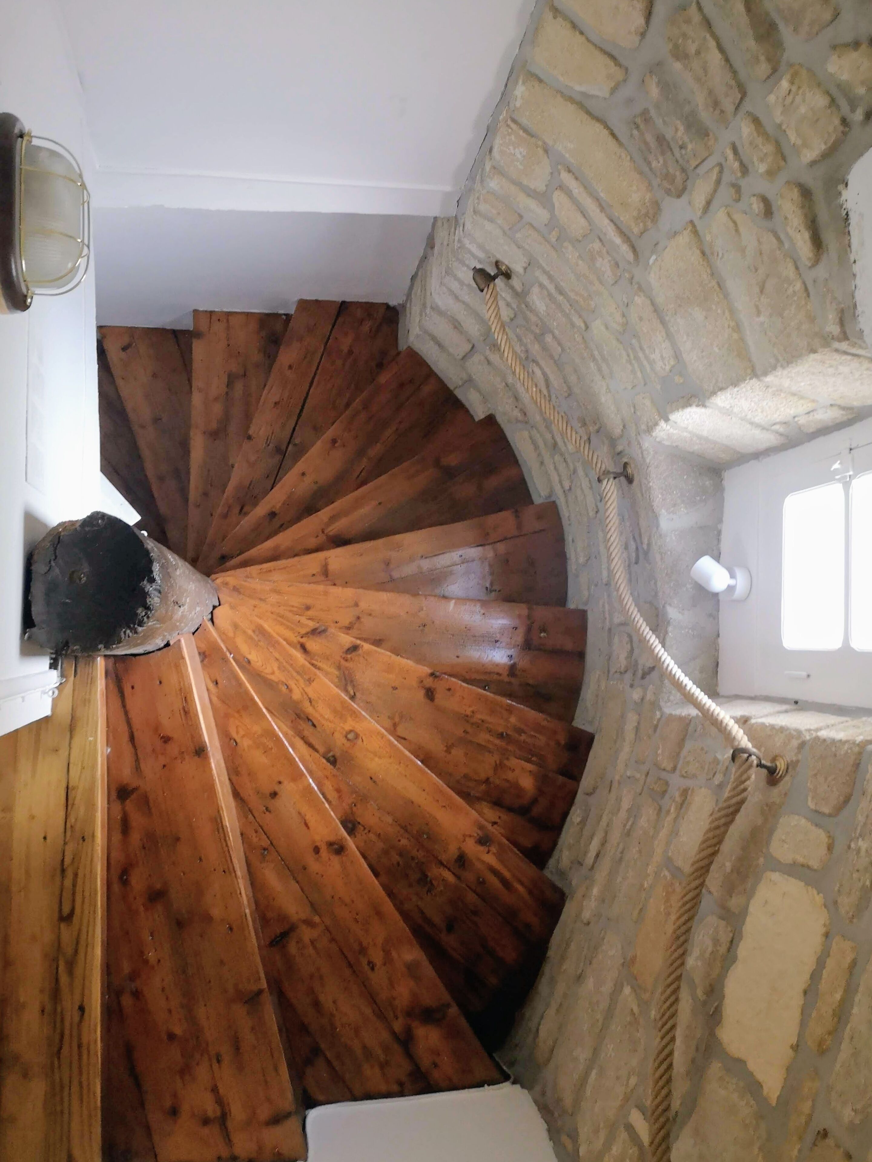A spiral staircase with wooden steps leading down to a stone wall.