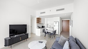 Una sala moderna con televisor de pantalla plana, un sofá, una mesa de comedor y una cocina al fondo.