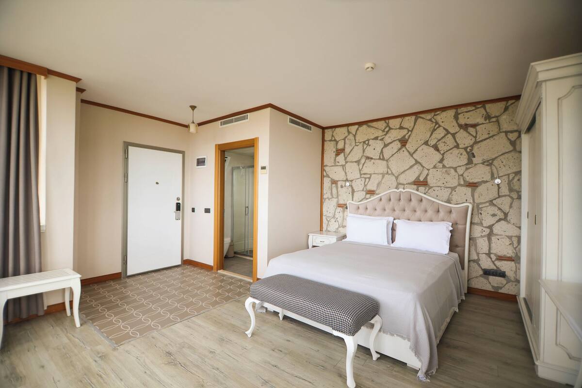Un dormitorio con una cama grande, un banco, un armario y una pared de piedra.