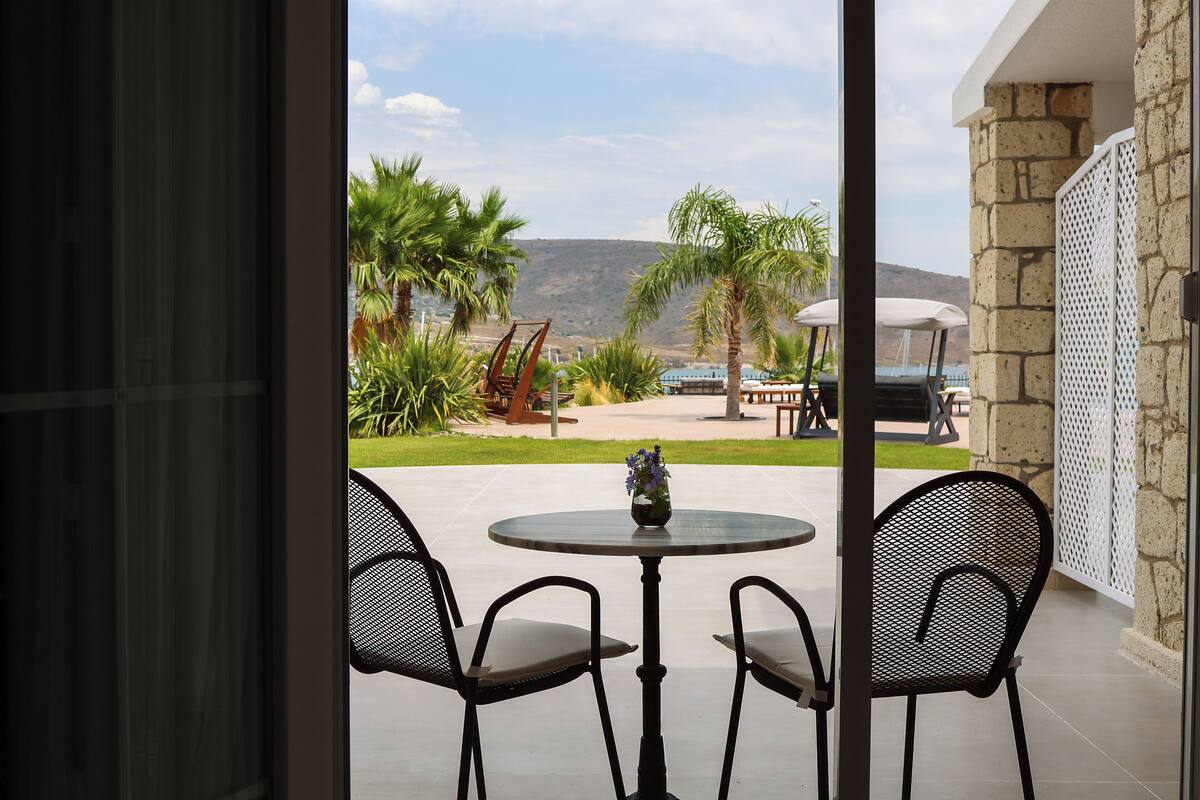Un patio al aire libre con una mesa redonda y dos sillas, con vistas a un paisaje pintoresco con palmeras y una montaña a lo lejos.